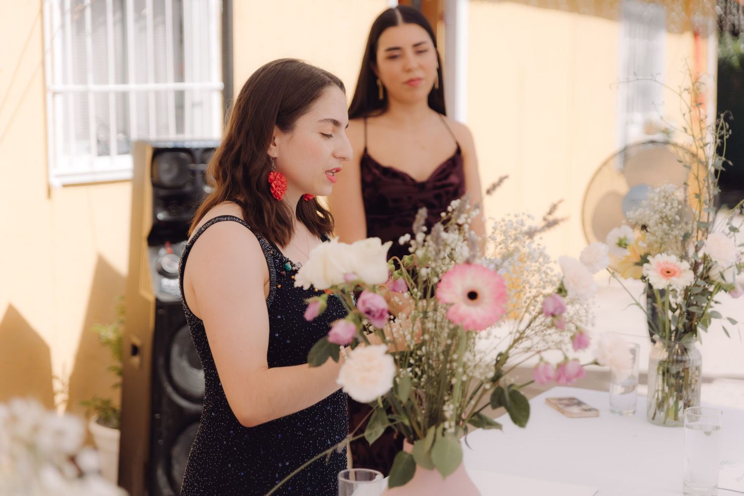 Woman in black dress arranges floral centerpiece at outdoor wedding reception table.