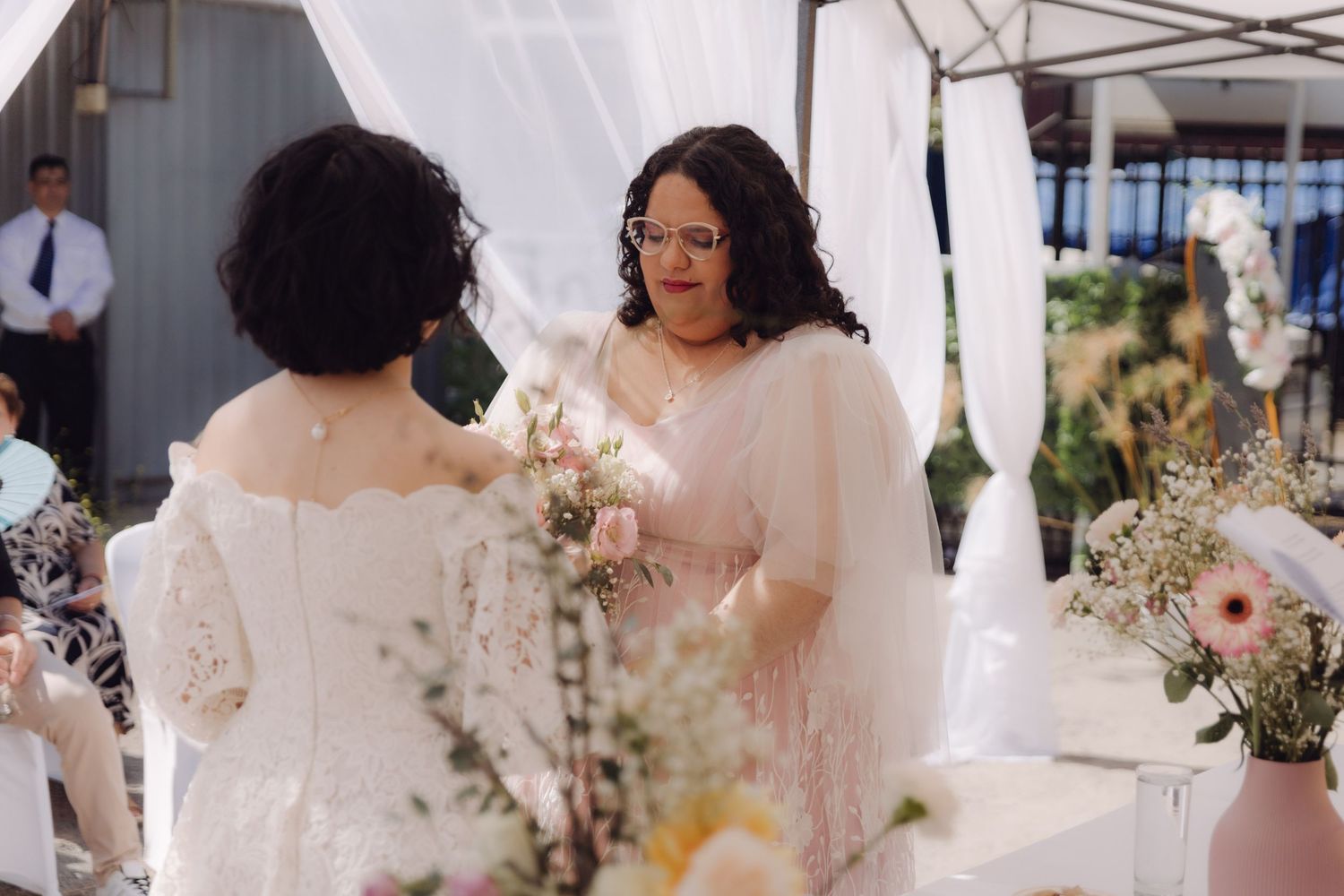 Two brides share intimate moment at outdoor wedding altar adorned with fresh flowers.