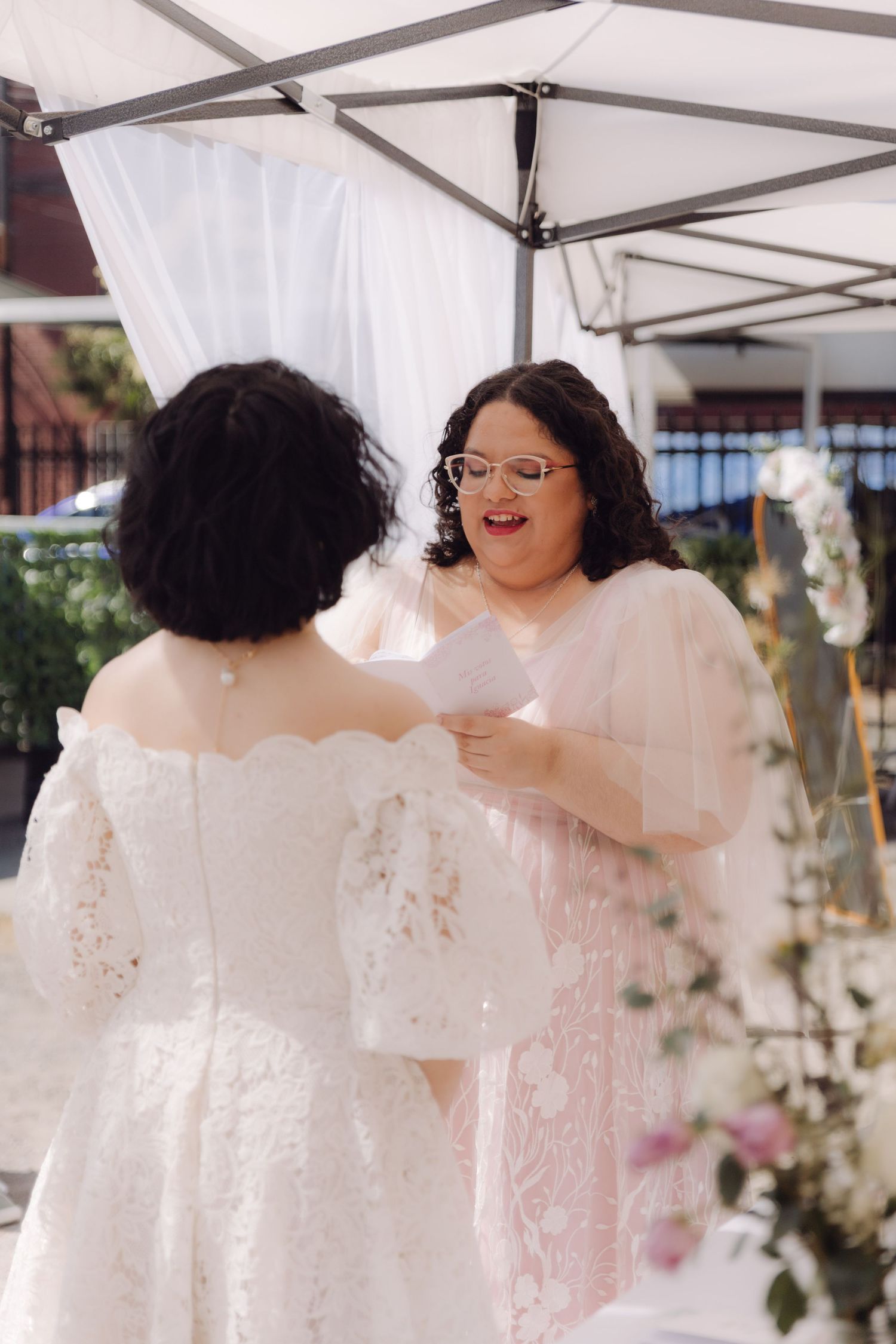 Bride reads heartfelt wedding vows to her partner during an intimate outdoor ceremony under a white tent.