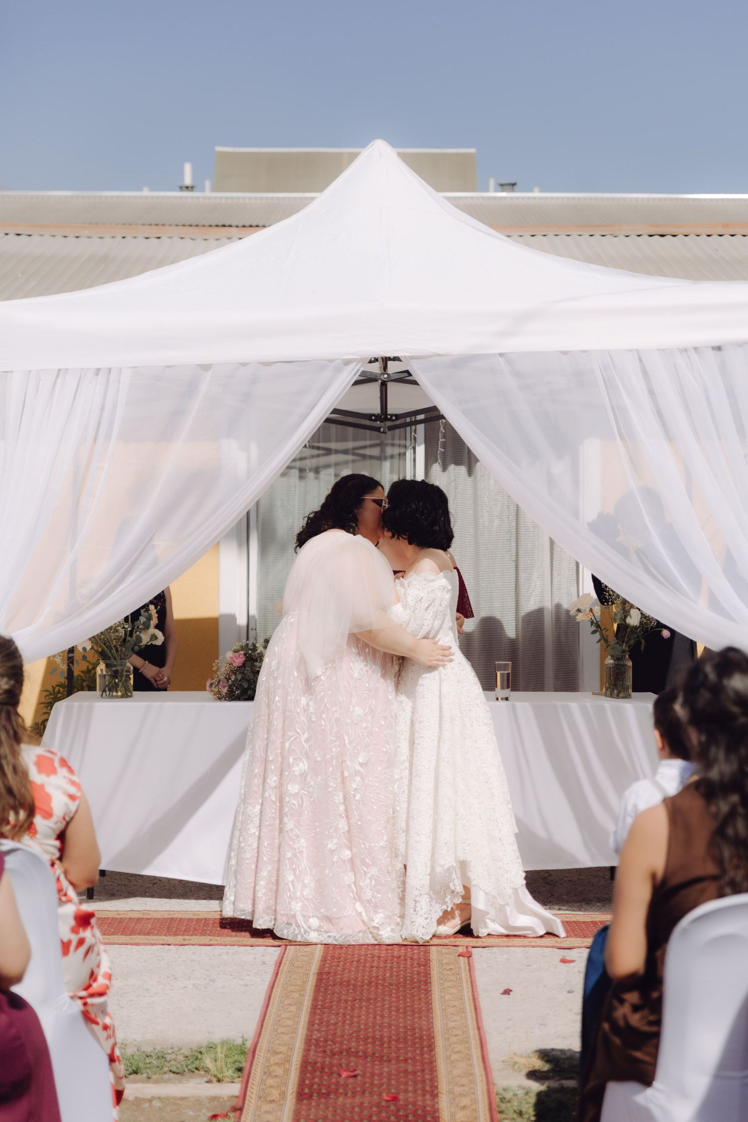 Newlywed couple shares a romantic first kiss under a white draped tent at their wedding.