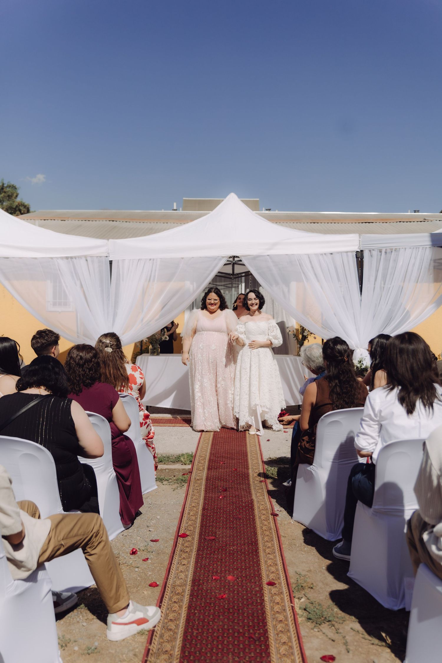 Two brides walk hand in hand down the aisle after their outdoor wedding ceremony.