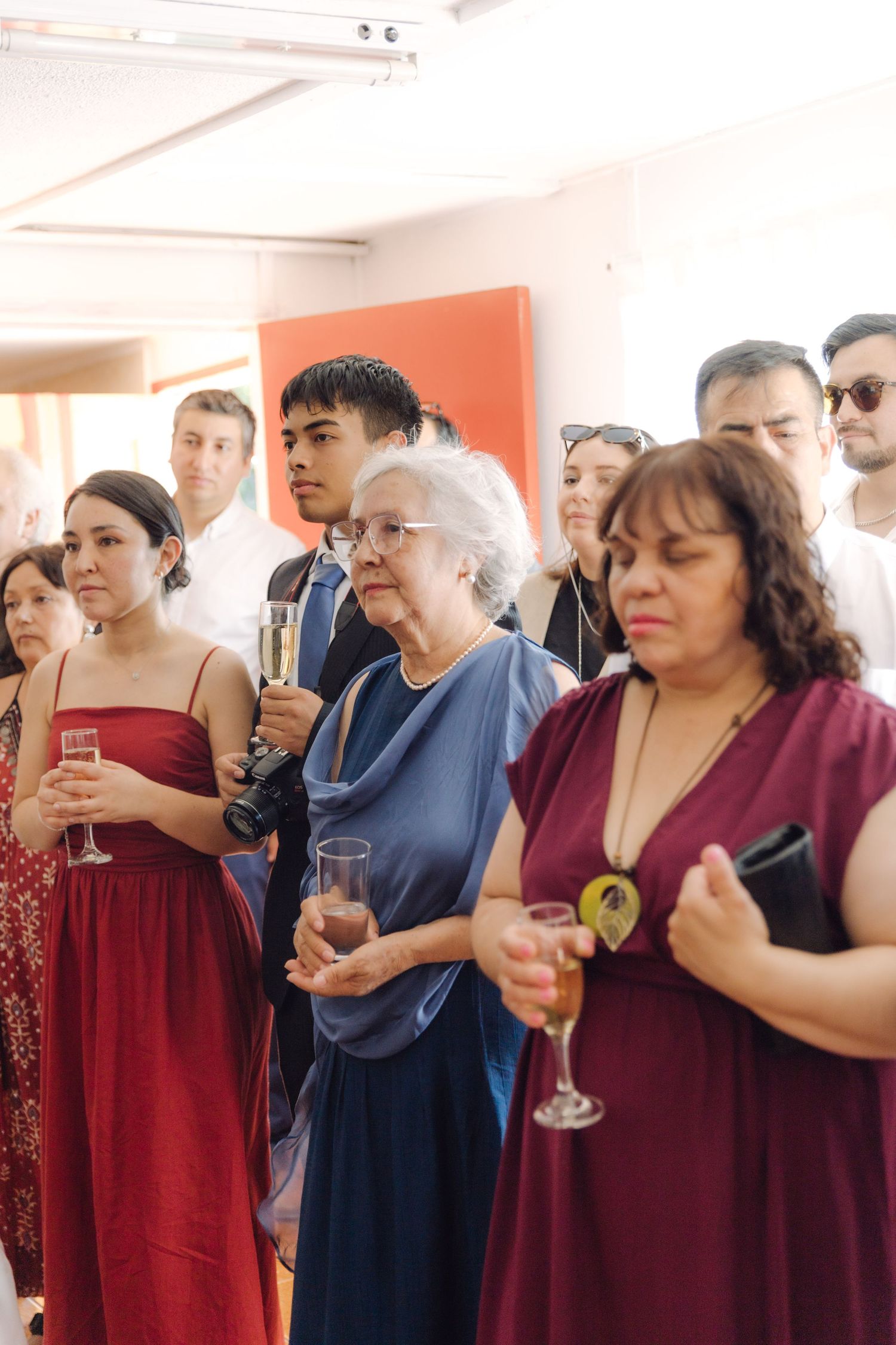 Wedding guests in formal attire hold champagne glasses during a reception ceremony indoors.