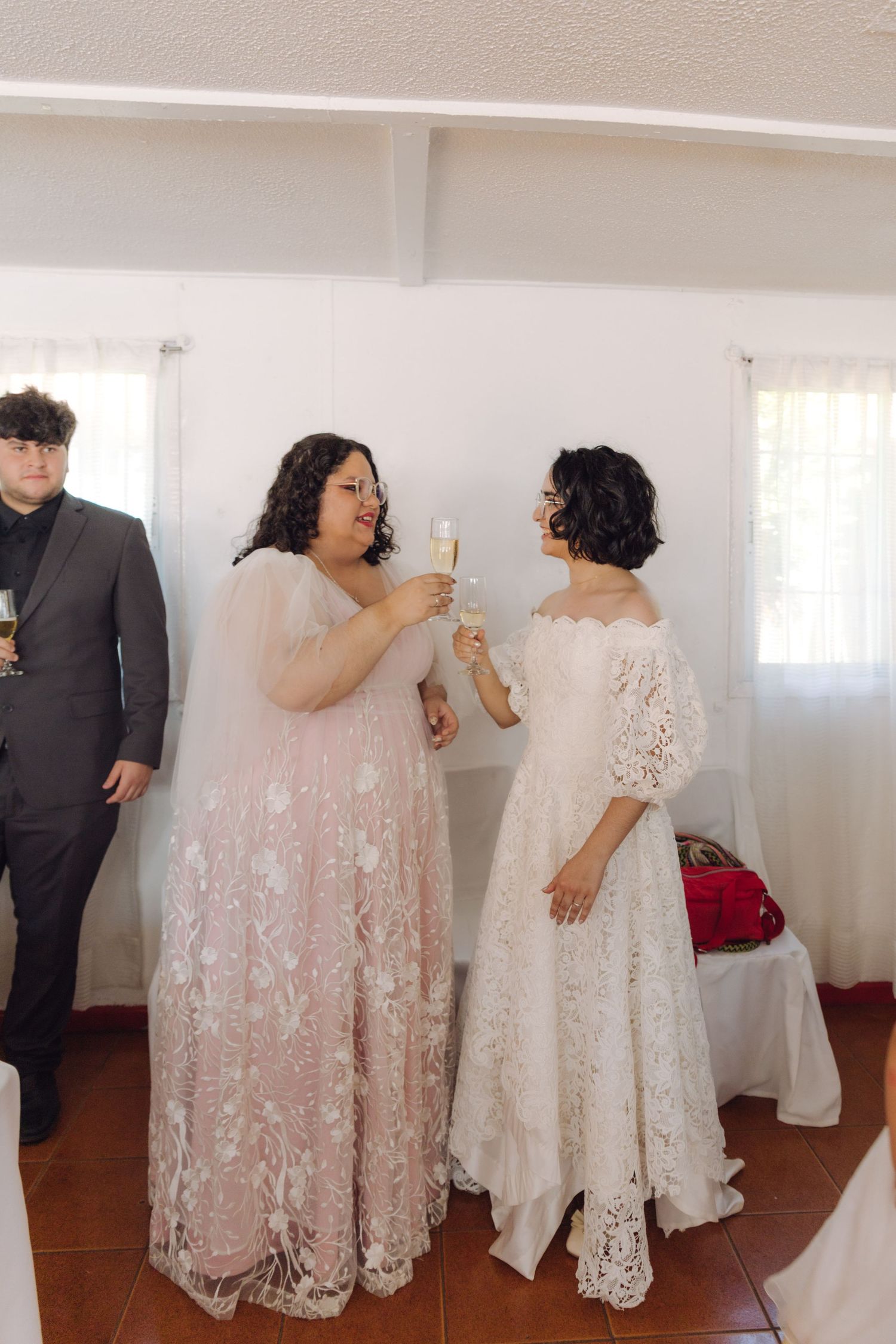 Two brides in lace wedding gowns toast with champagne glasses at their wedding reception.