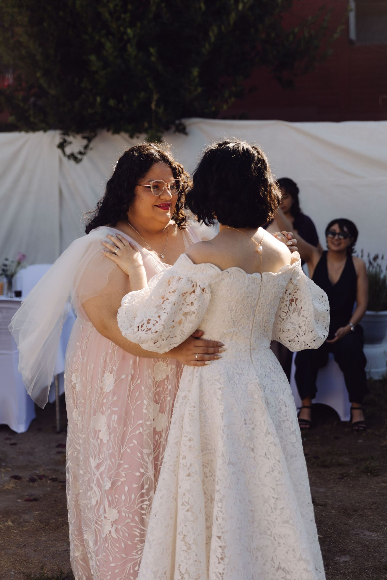 Two brides sharing intimate dance moment at outdoor wedding reception with guests in background.