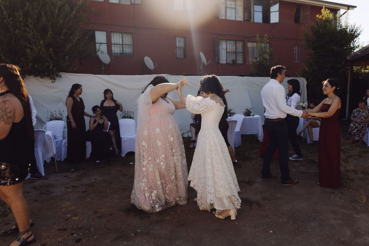 Two brides dance together at outdoor wedding reception with guests watching in background.