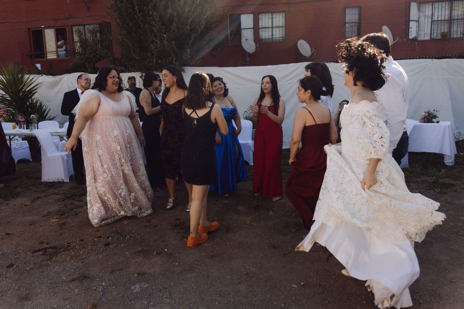 Bride in white lace gown dances with wedding guests at outdoor reception celebration.