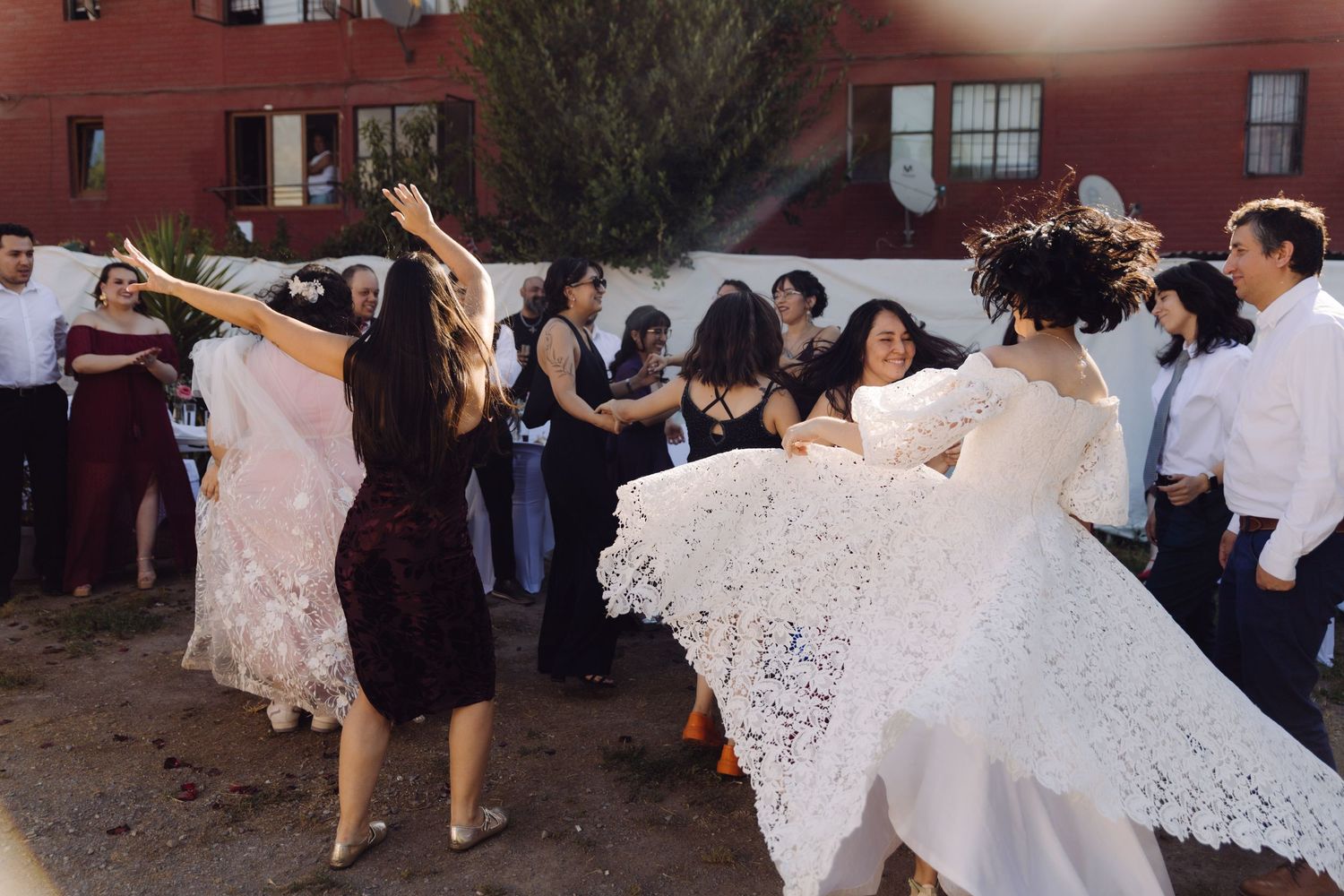 Bride in white lace gown twirls with wedding guests during lively outdoor reception dance.