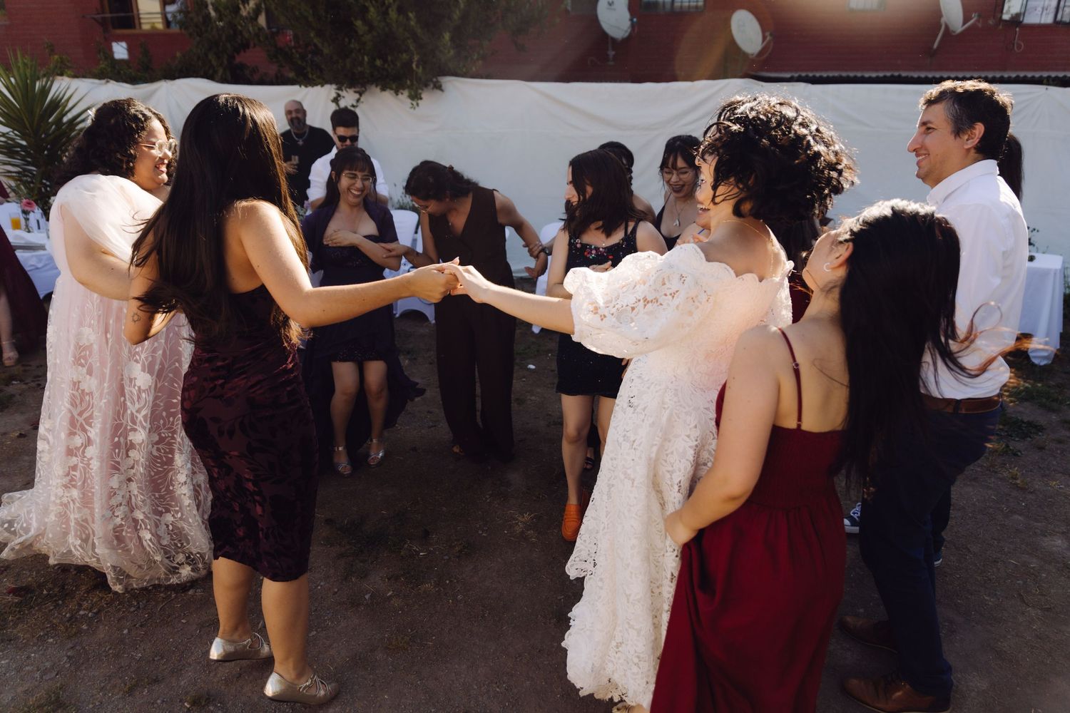 Bride in white puff-sleeve gown dances with guests at outdoor evening wedding reception.