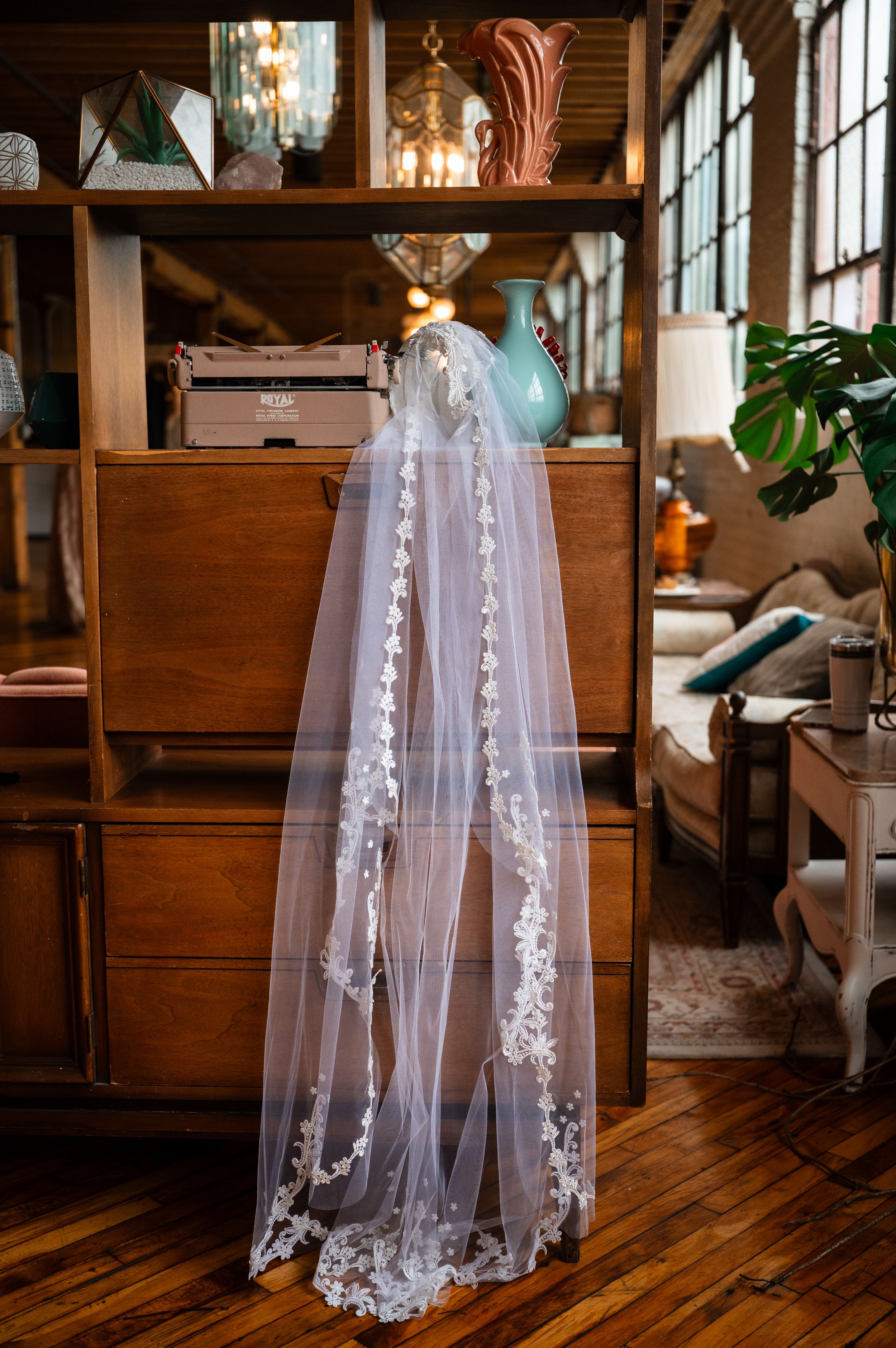 Elegant lace-trimmed wedding veil draped over vintage wooden furniture in a warmly decorated bridal suite.