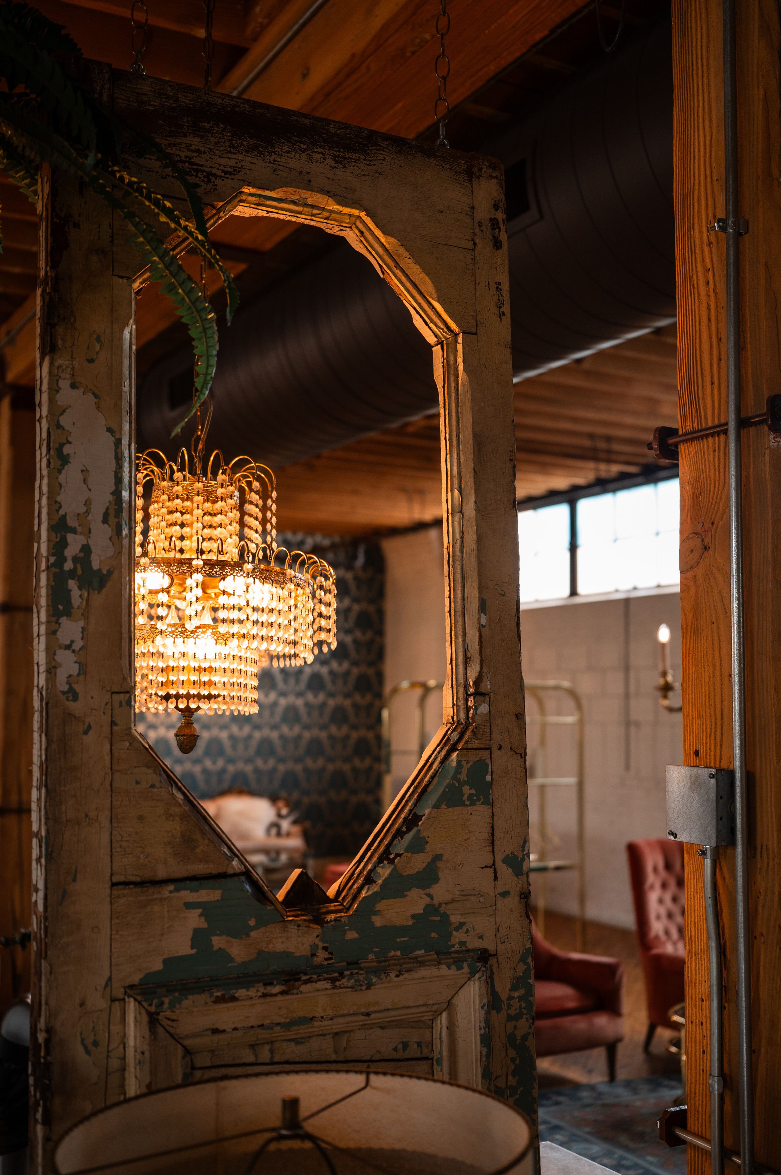 Vintage gold octagonal mirror reflecting an ornate crystal chandelier in a rustic, warmly lit interior space.