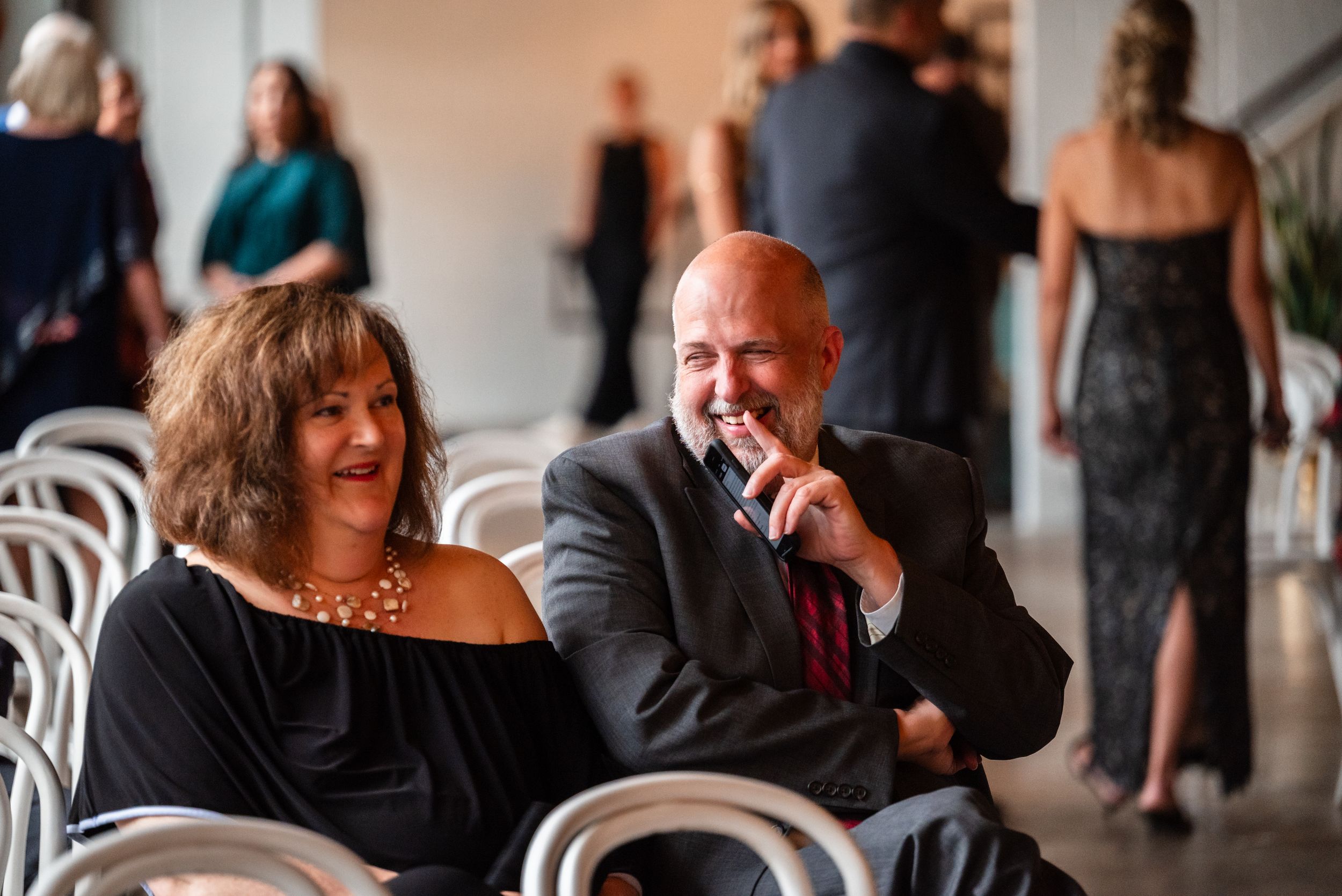 A smiling couple in formal attire shares a joyful moment seated at a wedding reception venue.