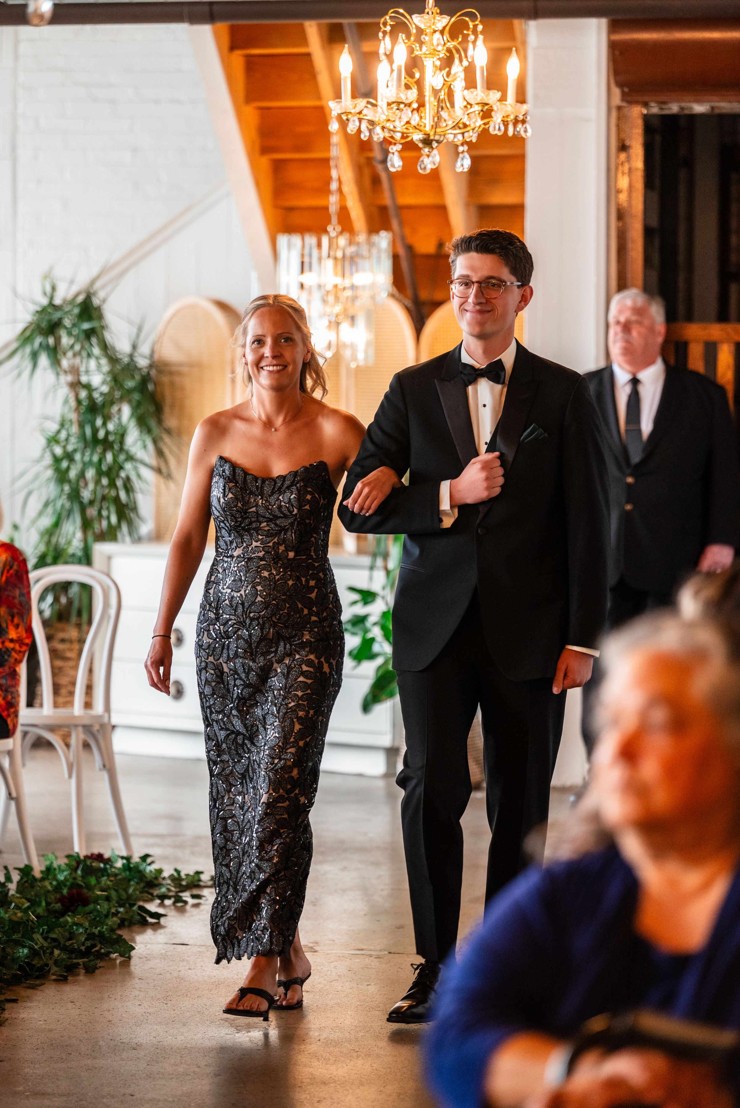 Elegant wedding processional with woman in black lace gown and man in tuxedo walking down the aisle.