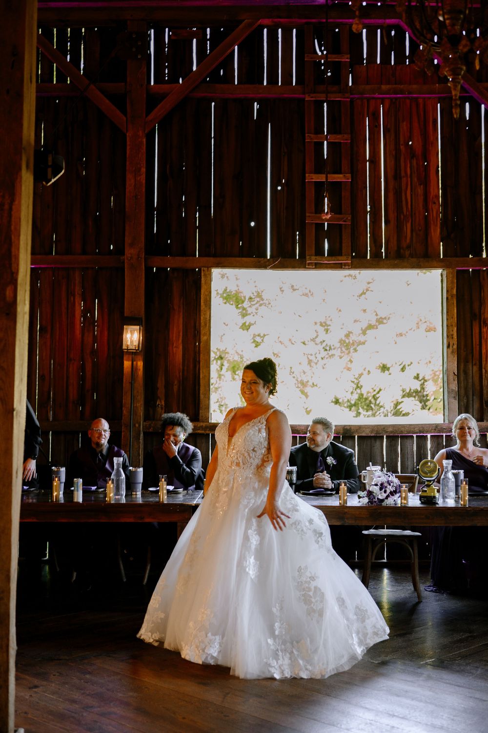Bride in lace ball gown twirls on dance floor of rustic wooden barn wedding reception venue.