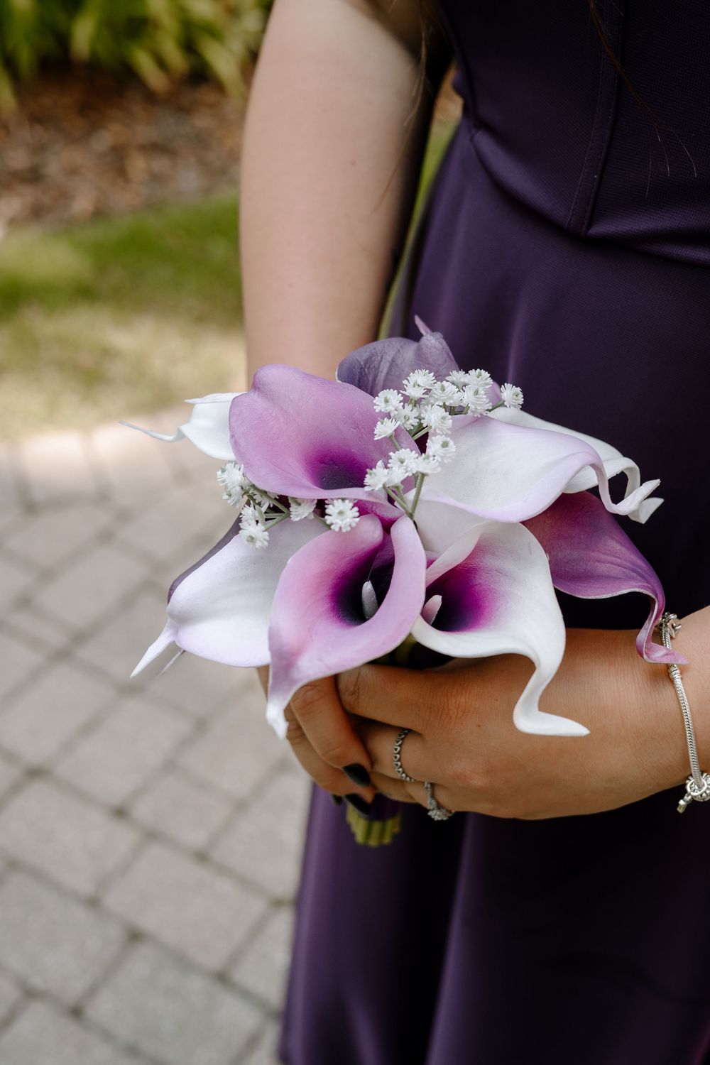 Bridesmaid in purple dress holding a bouquet of white and purple calla lilies with baby's breath accents.