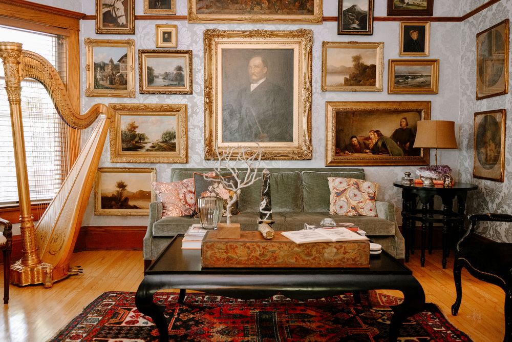 Elegant living room with gallery wall of paintings, gold harp, velvet sofa, and Persian rug in a classic interior.