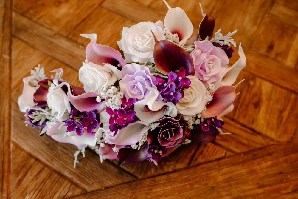 Elegant wedding bouquet featuring purple calla lilies, white roses, and violet blooms on wood floor.