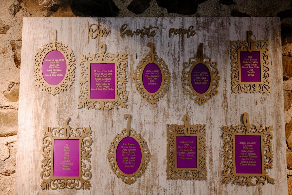 Gold ornate frames with purple inserts on a rustic wooden wedding seating chart display.