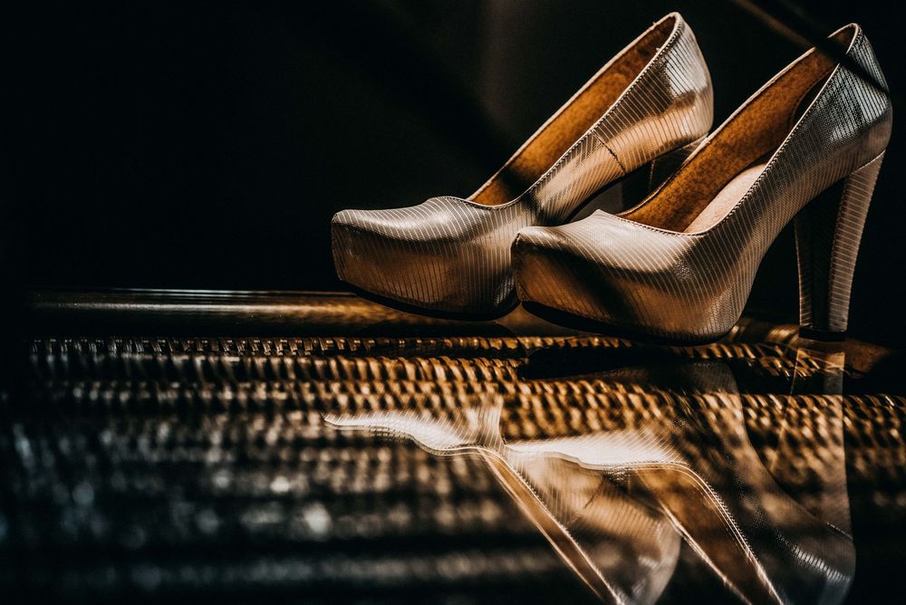 Elegant gold high heel shoes with platform soles displayed on a reflective dark surface in dramatic lighting.