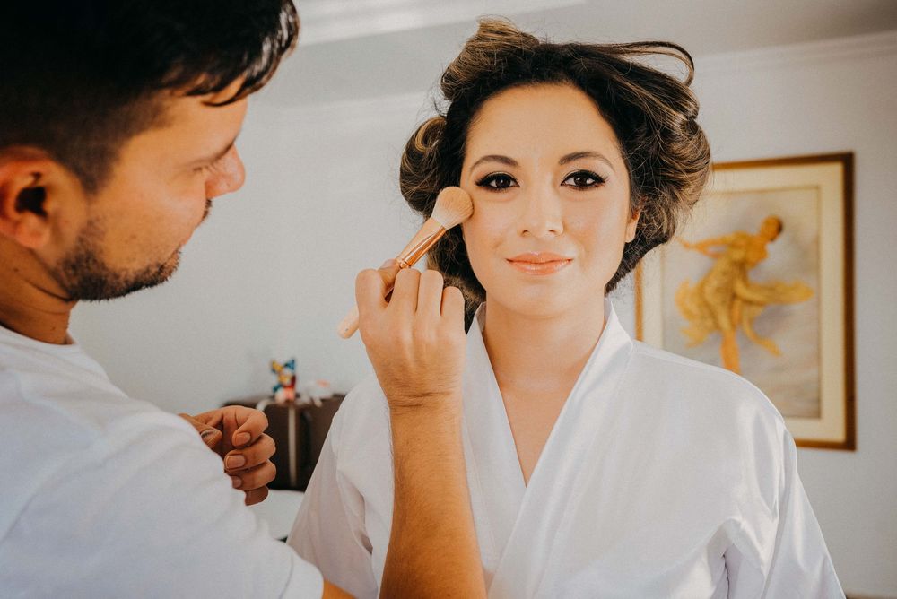 Professional makeup artist applying blush to a bride in a white robe on her wedding day.