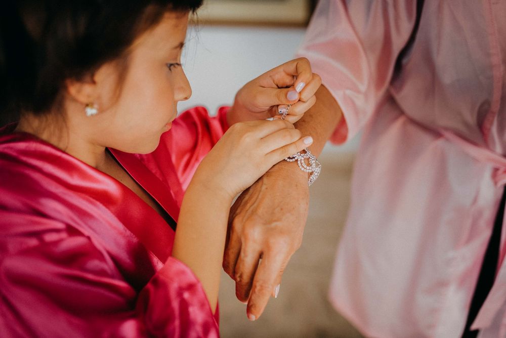 Young girl in pink robe admiring a diamond ring on a woman's hand during wedding preparations.