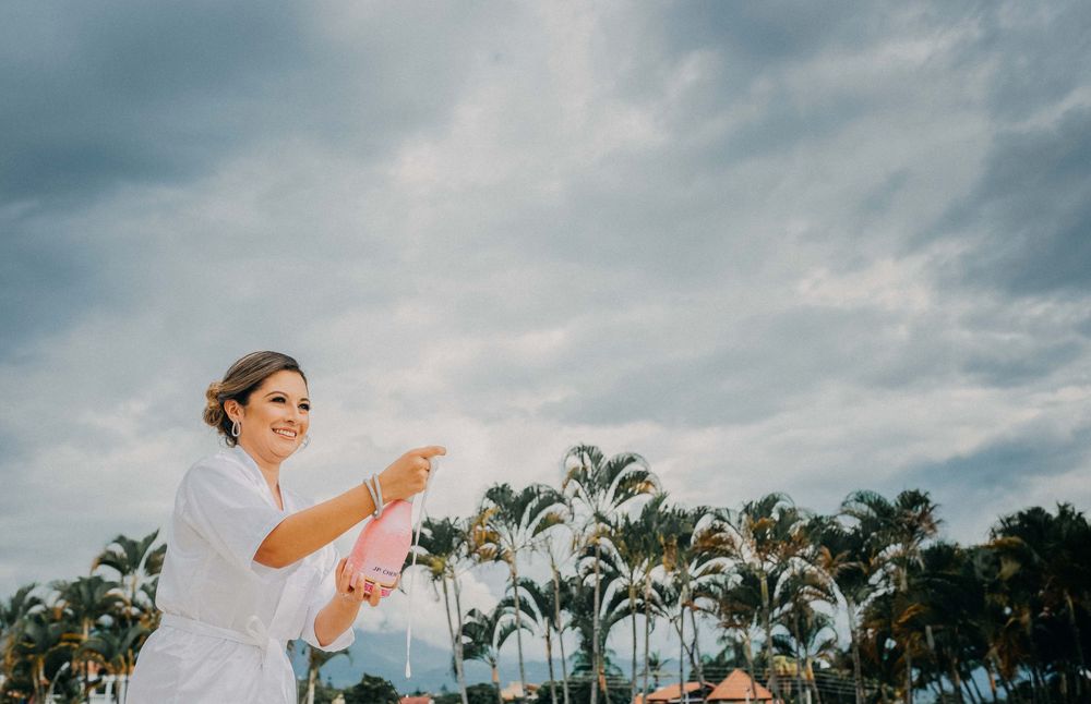 Smiling woman in white dress releasing a pink balloon among tropical palm trees under a cloudy sky.