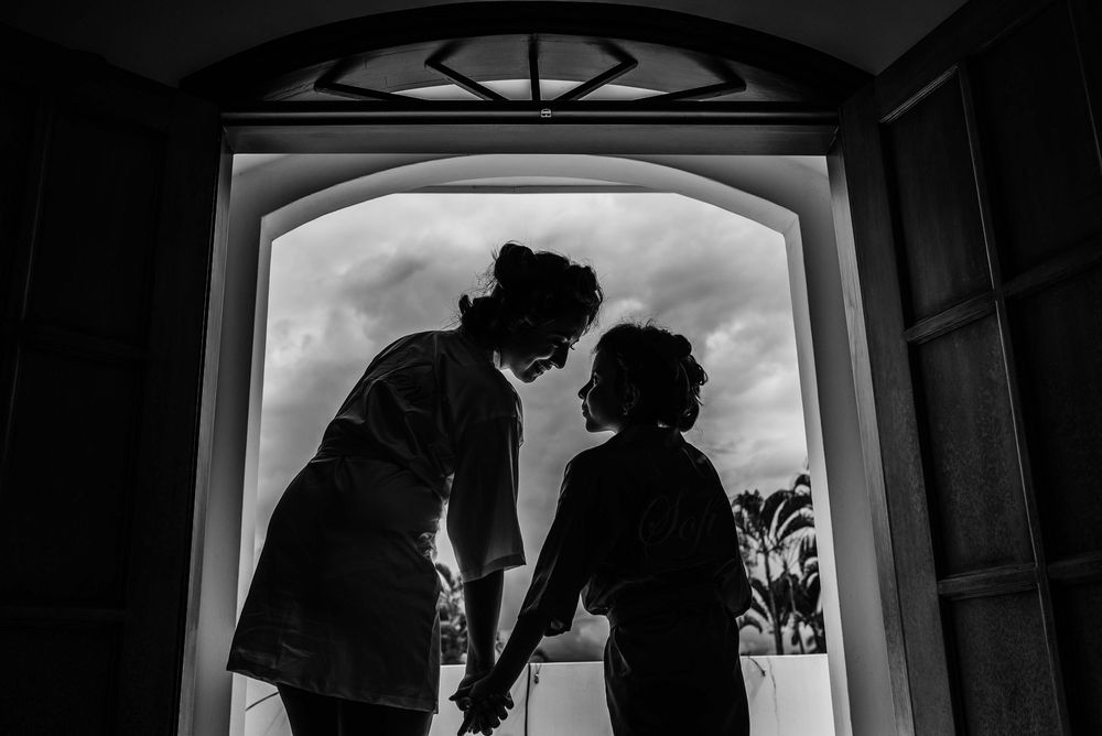 Black and white silhouette of two people holding hands in an arched doorway with cloudy sky backdrop.