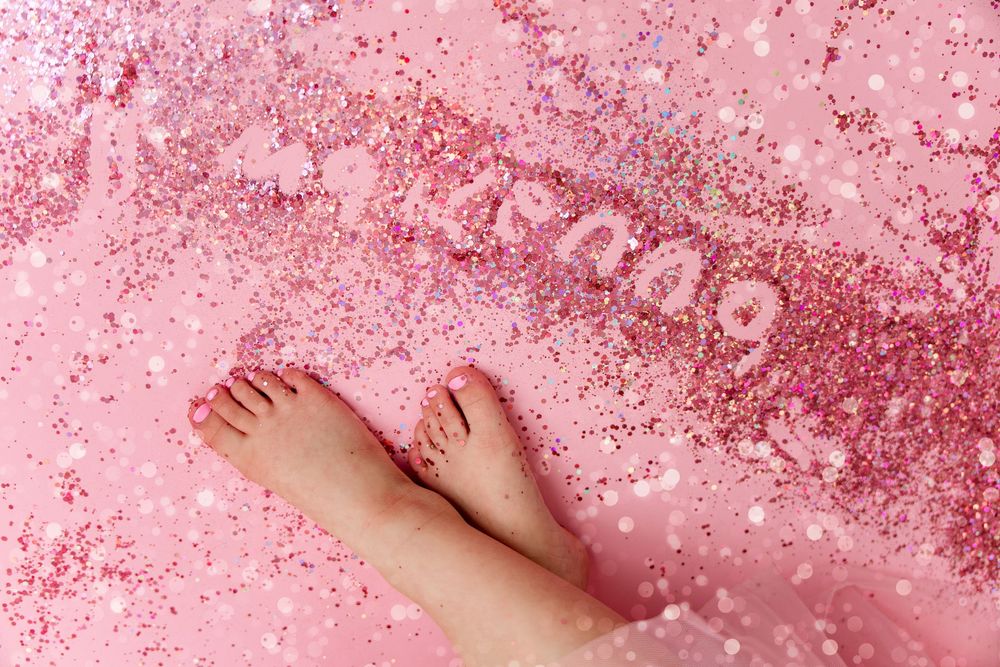 A smiling baby girl in a pink tutu dress crawls on a cream floor surrounded by pink and white balloons and bow decorations.
