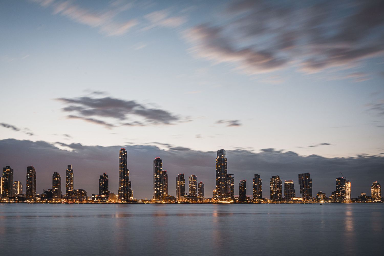 Skyline di grattacieli sul fiume al tramonto con cielo nuvoloso