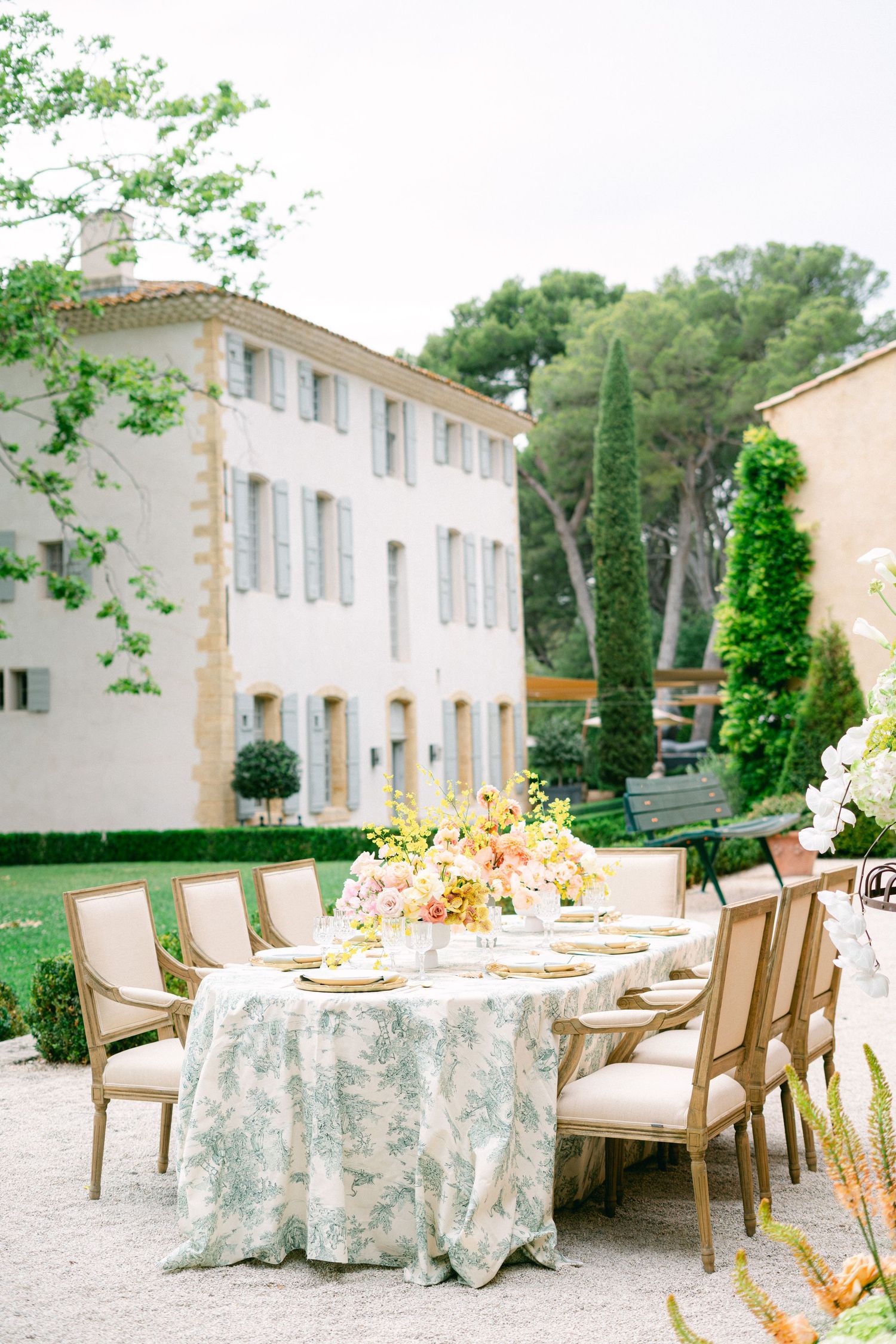 Elegant outdoor wedding reception table with floral tablecloth and pink centerpieces at a French chateau venue.