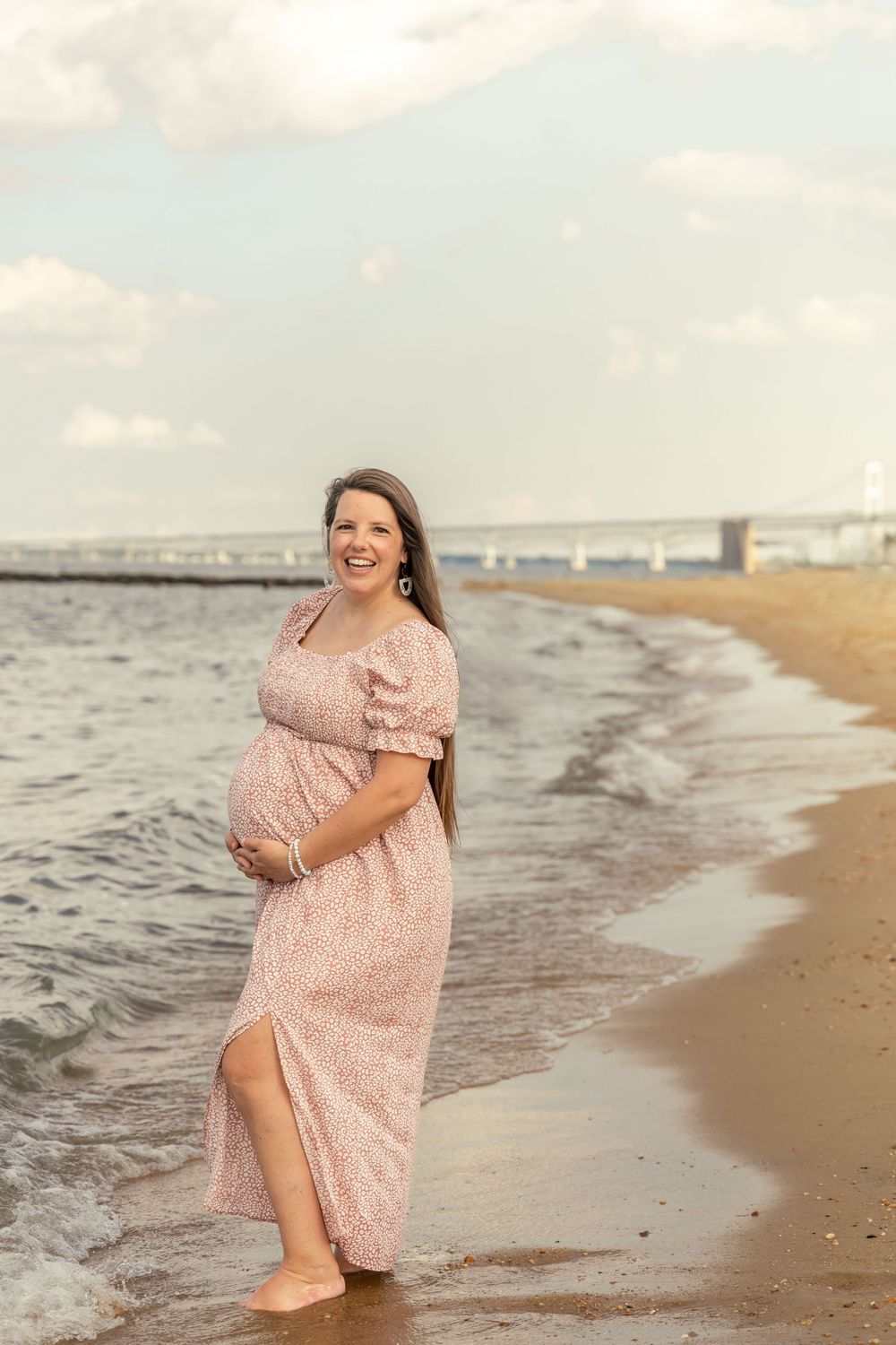 Maternity photoshoot on the beach at Sandy Point Park. Mom-to-be standing on the beach with waves crashing at her feet