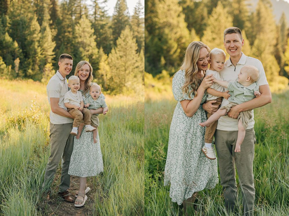 Family portrait in a sunlit meadow with tall green grass and pine trees, parents holding a baby in neutral tones.