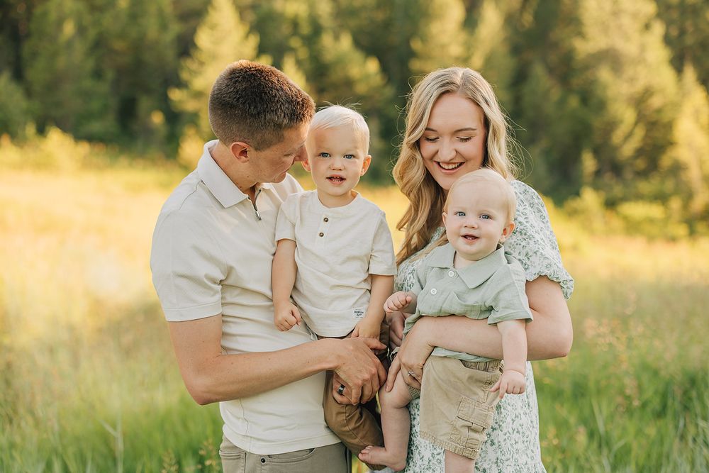 Happy family with two toddler boys posing outdoors in a sunny green meadow during a professional photo session.
