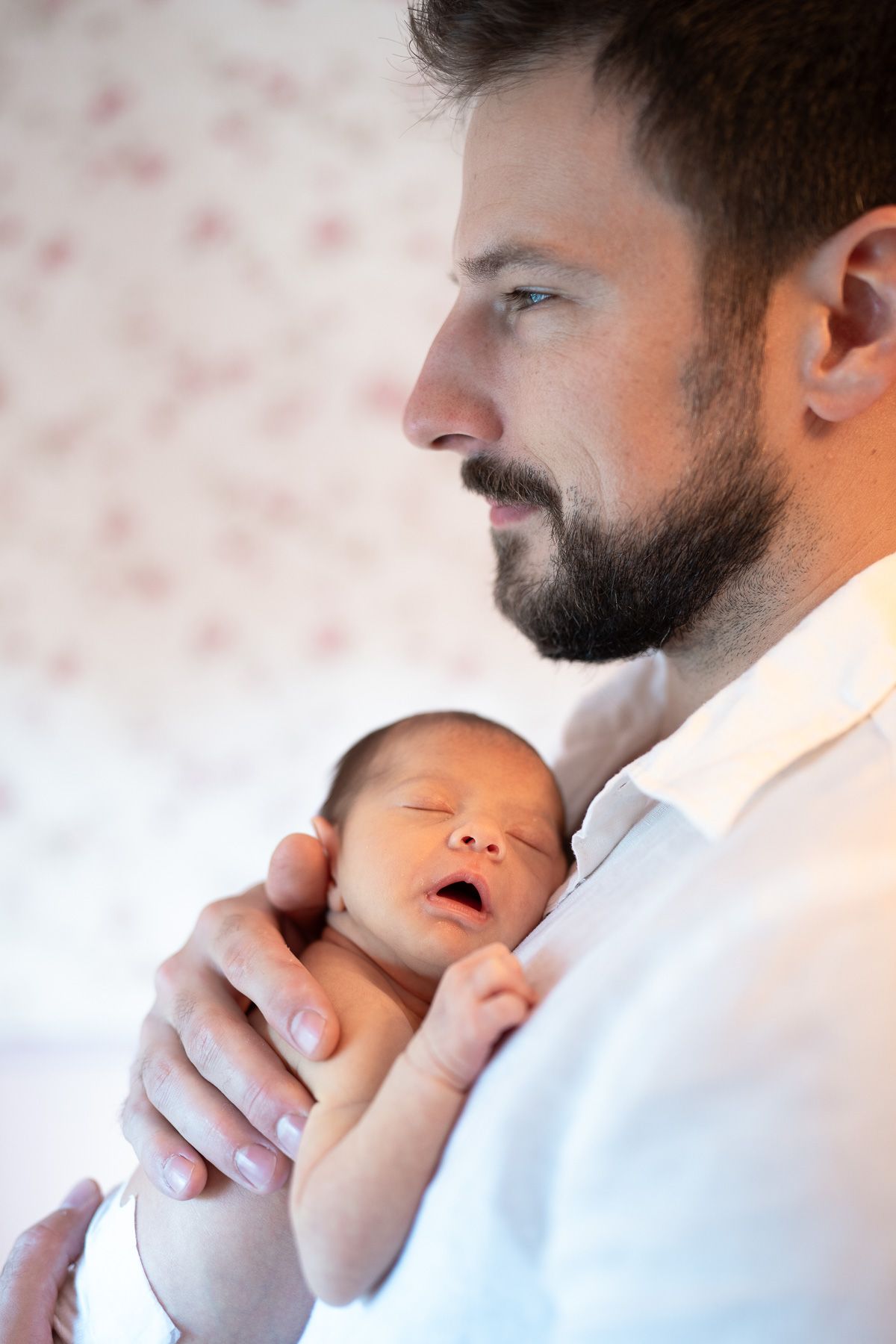 A tender moment shows a man in white holding a sleeping newborn baby against his chest during lifestyle newborn session in Mount Prospect.