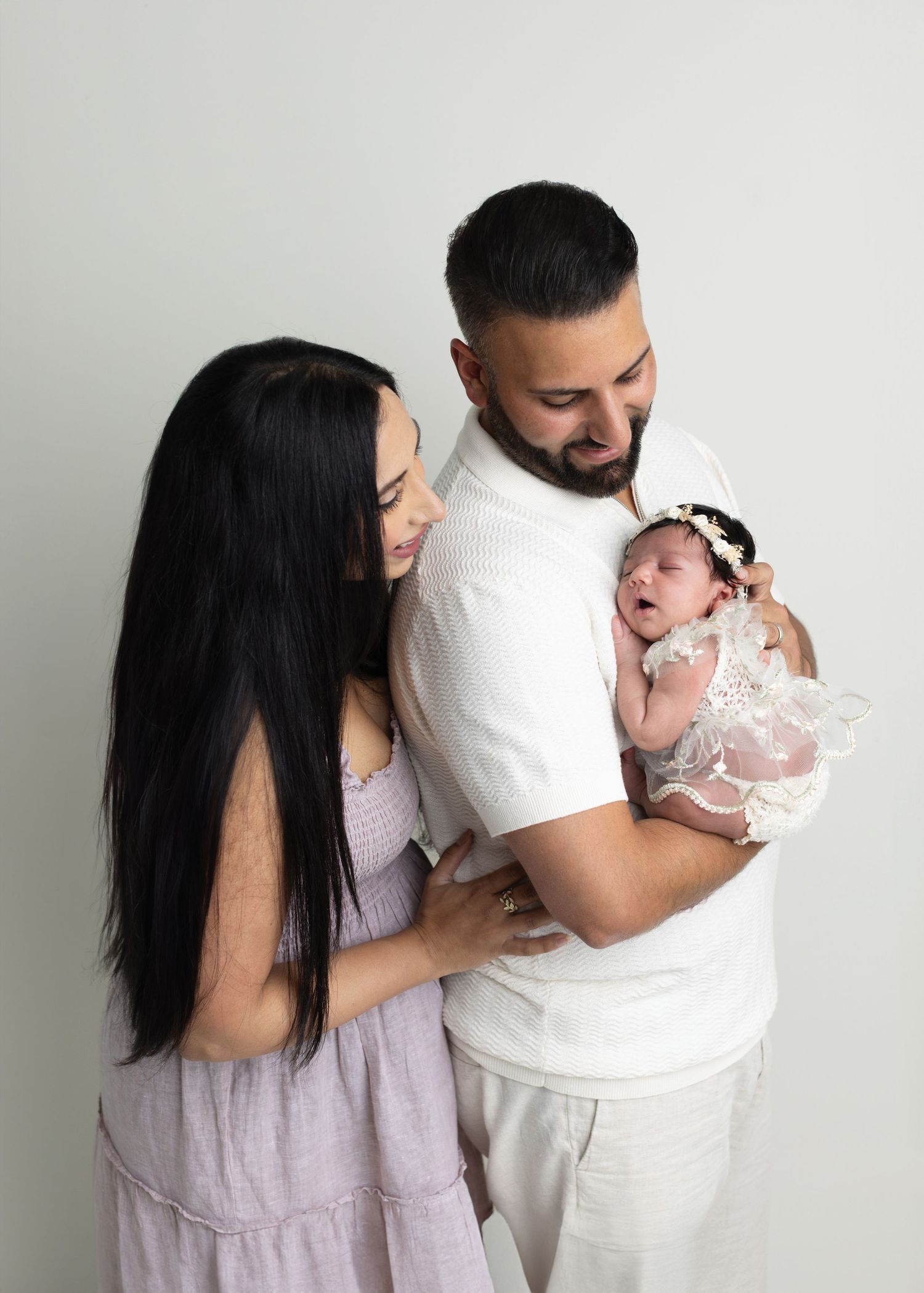 New parents lovingly gaze at their newborn baby girl in a soft studio portrait.