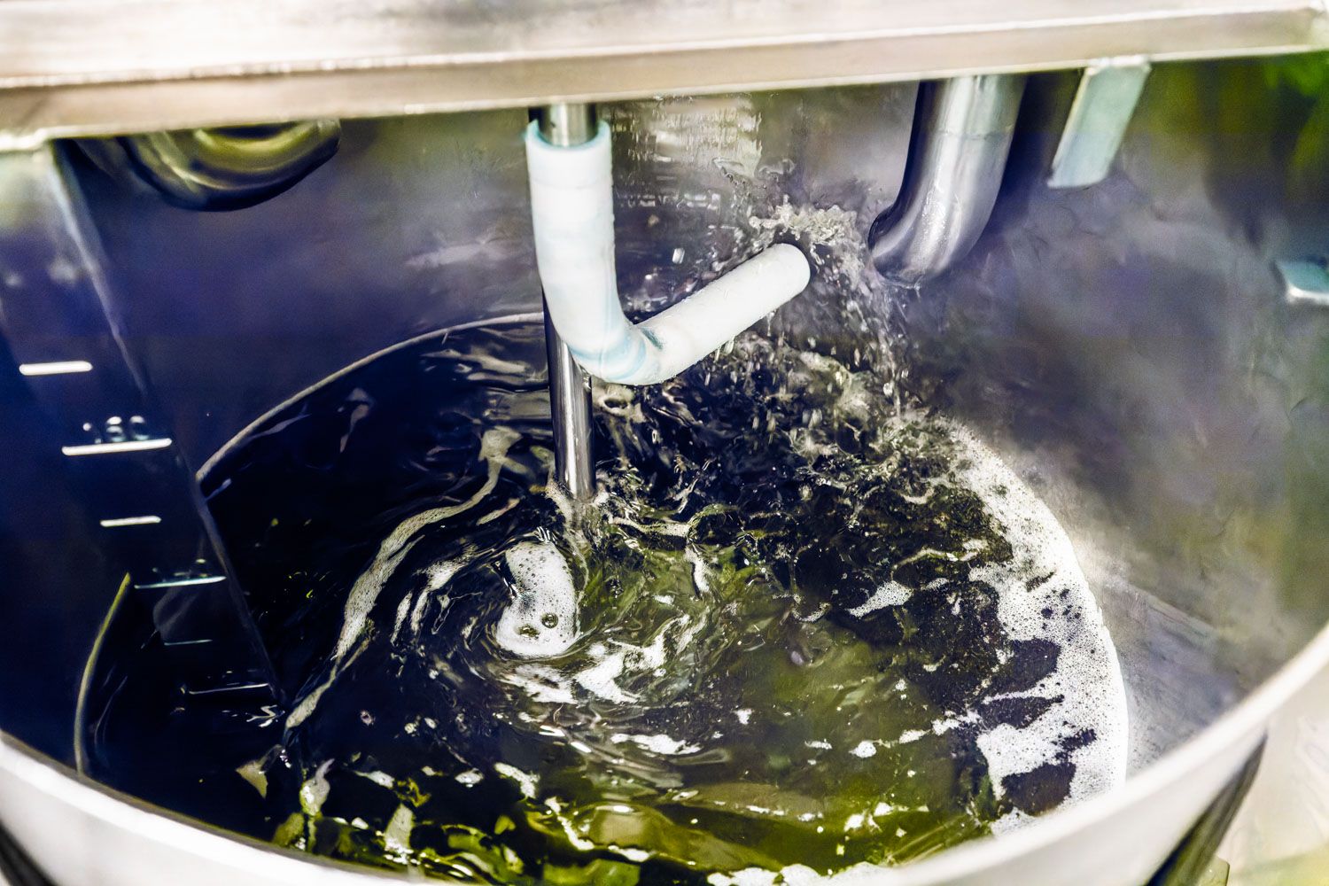 Industrial mixing tank with dark liquid being agitated by a mechanical stirrer in a stainless steel vat.