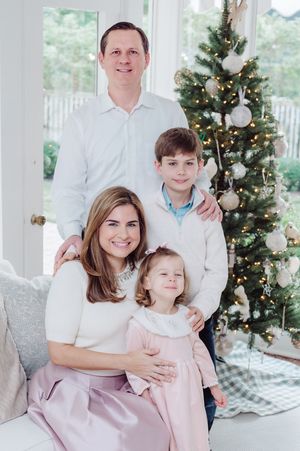 Family of four posing for a Christmas portrait near a decorated tree with white and gold ornaments.