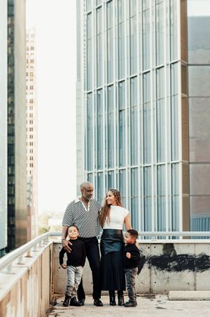 A stylish family of four poses together on an urban rooftop with modern skyscrapers in the background.