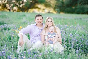 Family of three sitting in a blooming wildflower field, smiling couple with baby on sunny day.