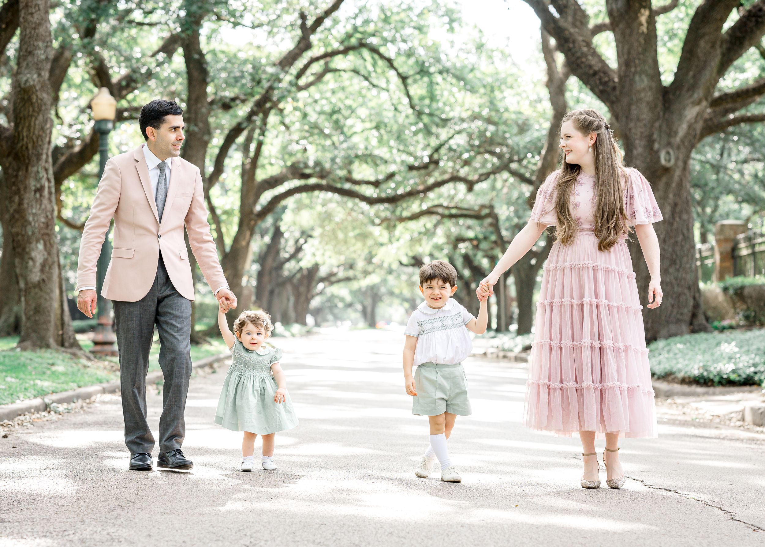 Family of four walking outdoors under oak trees, dressed in coordinating pink and mint pastel outfits.