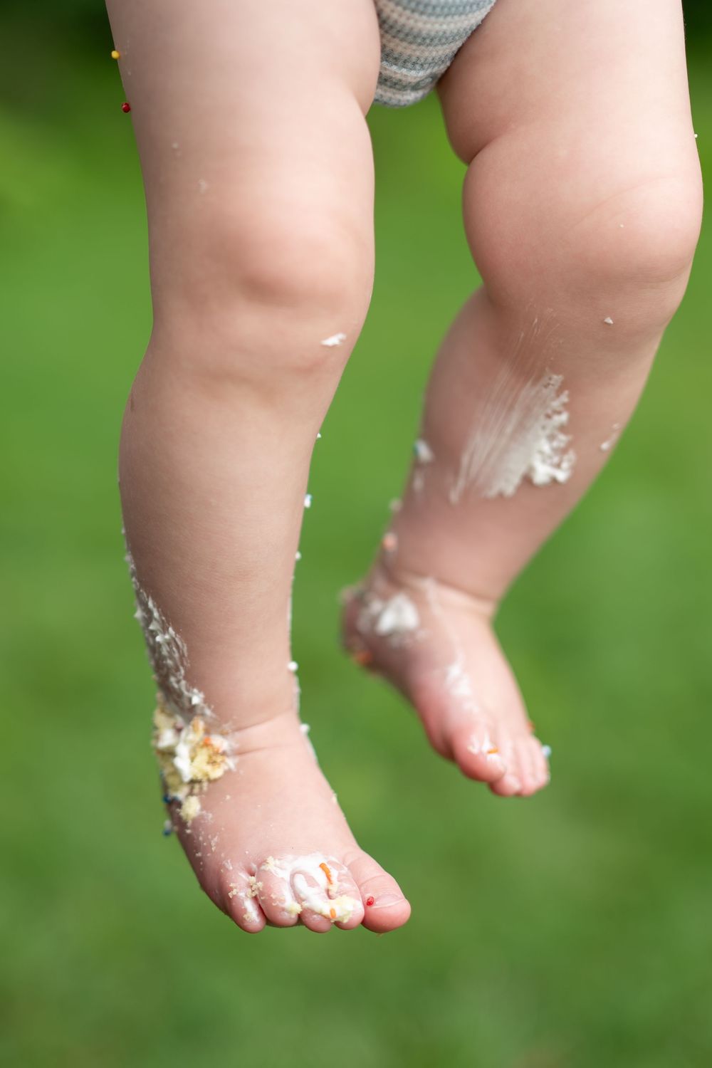 Close-up of a baby's chubby legs and feet covered in cake frosting during a smash cake celebration.