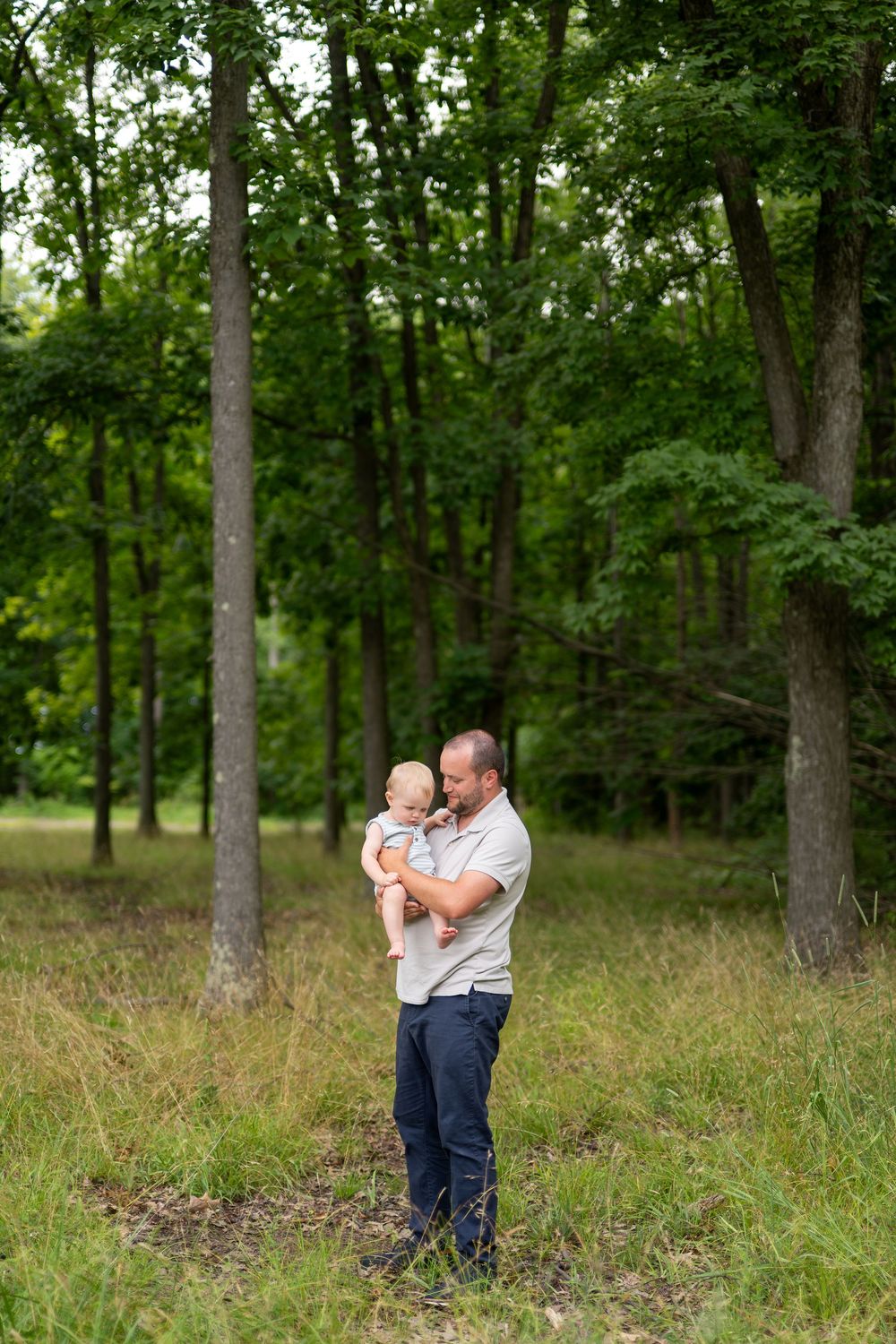 Father holding baby in lush green forest clearing, sharing a tender moment outdoors.