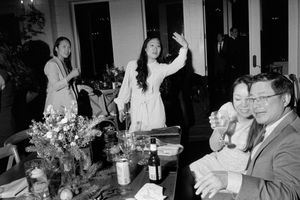 Black and white candid photo of wedding reception guests laughing and celebrating at dinner table.