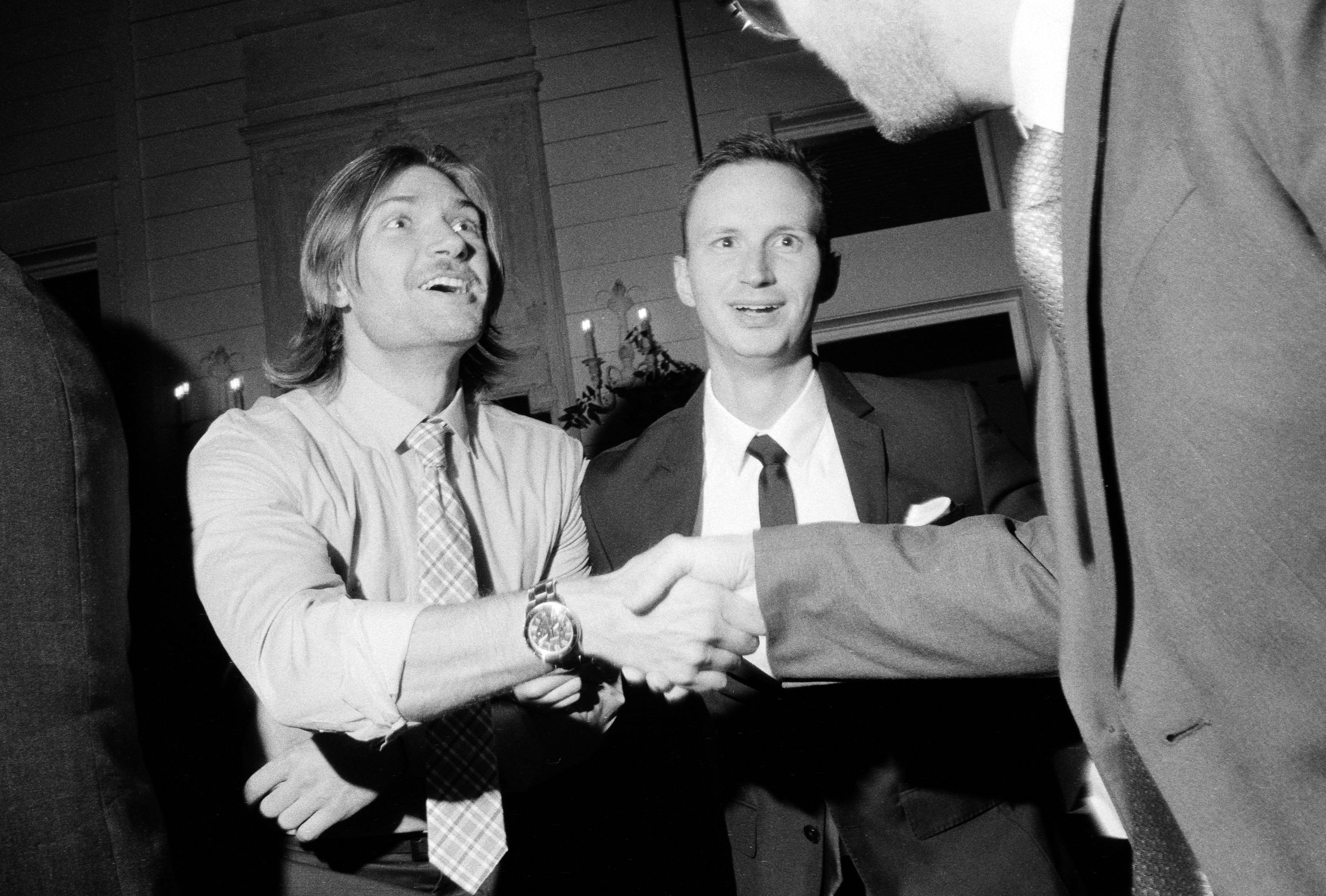 Black and white photo of two men smiling and shaking hands at a wedding reception.