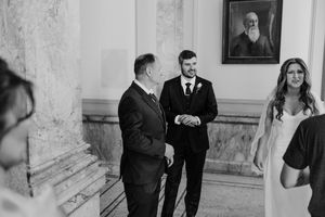 Groom in suit smiles warmly while greeting guests at elegant wedding ceremony venue.