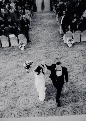 Aerial black and white photo of newlyweds walking down the aisle at their wedding ceremony.