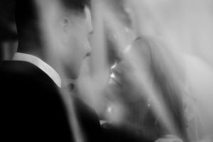 Black and white wedding photo of bride and groom sharing an intimate moment, veiled in soft light.