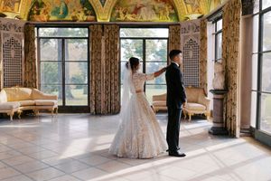 Bride and groom share first dance in elegant ballroom with ornate ceiling murals and tall windows.