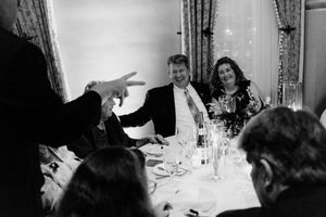 Black and white photo of guests laughing at a formal dinner table during an elegant wedding reception.
