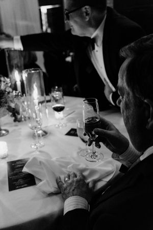 Black and white photo of a man holding a wine glass at an elegant candlelit dinner table during a formal event.