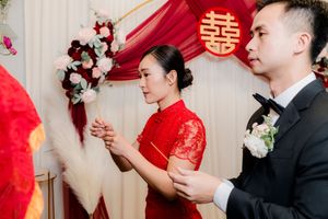 A bride in a red cheongsam and groom in a suit participate in a traditional Chinese wedding ceremony.